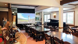 Zona de bar con piano, varias mesas y sillas, una pantalla de proyector y una vitrina para vinos.
