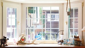 Una habitación con un ventanal grande, una mesa de madera con varios objetos decorativos y una planta colgante.