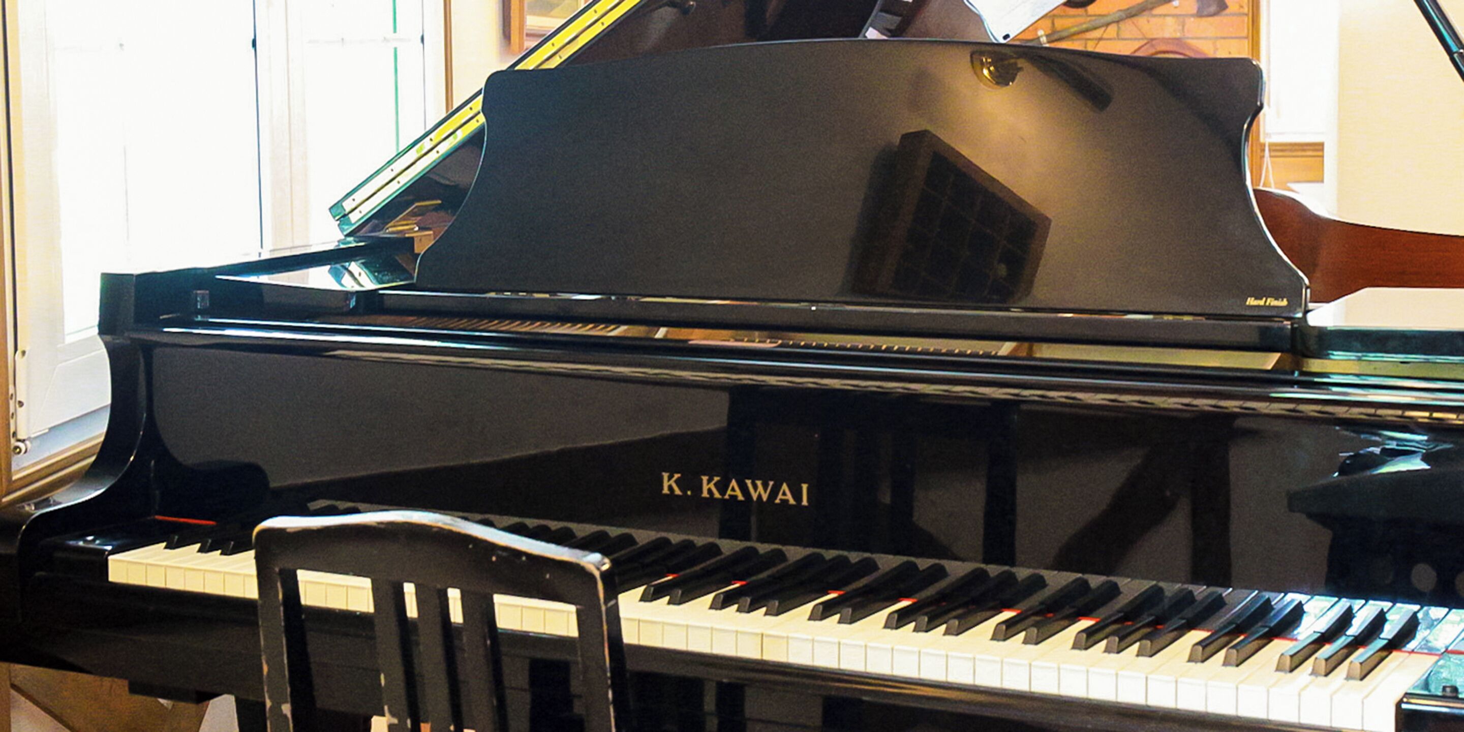 A Kawai grand piano with a wooden chair in front.