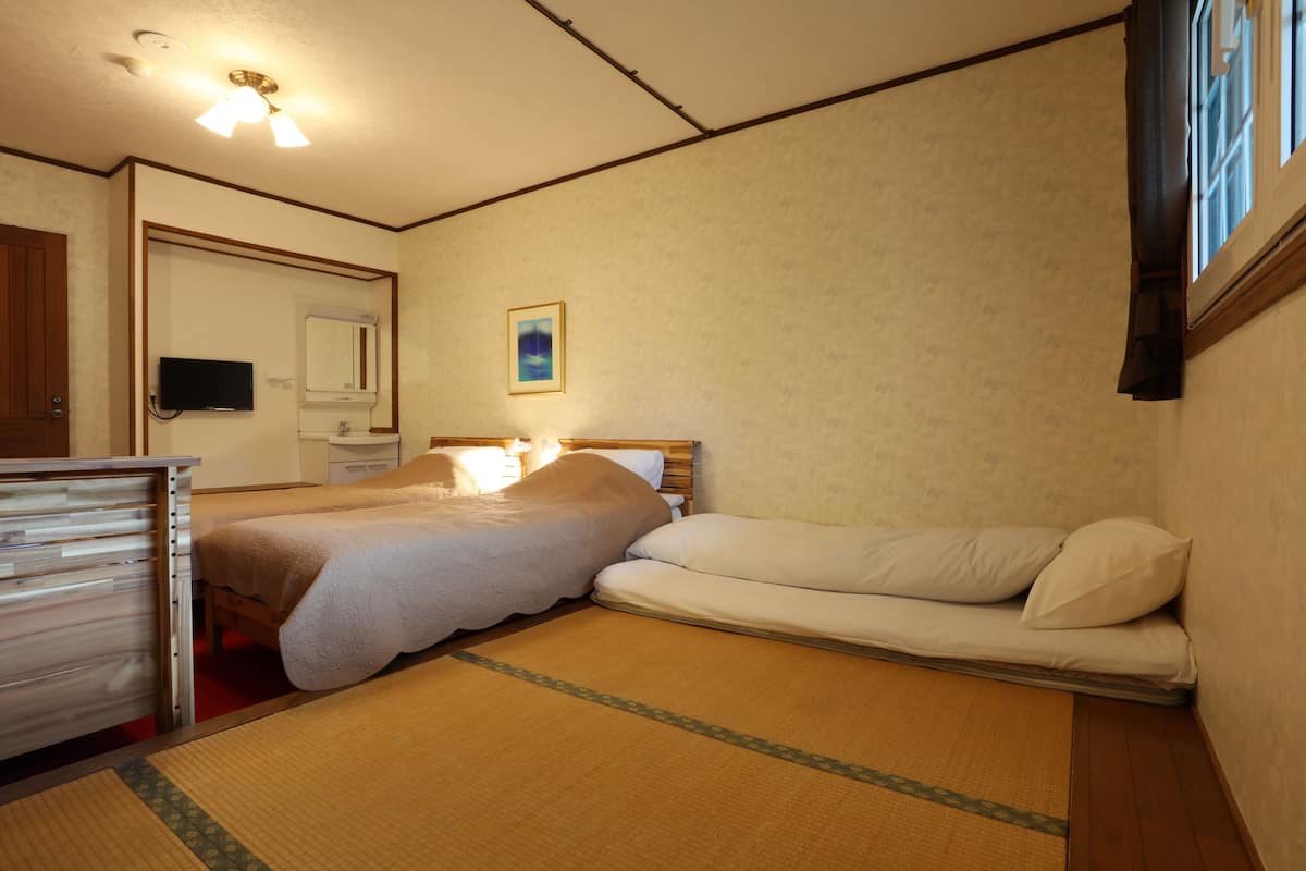 A room with a bed, a bedside table, a mirror, a television, and a window with curtains.
