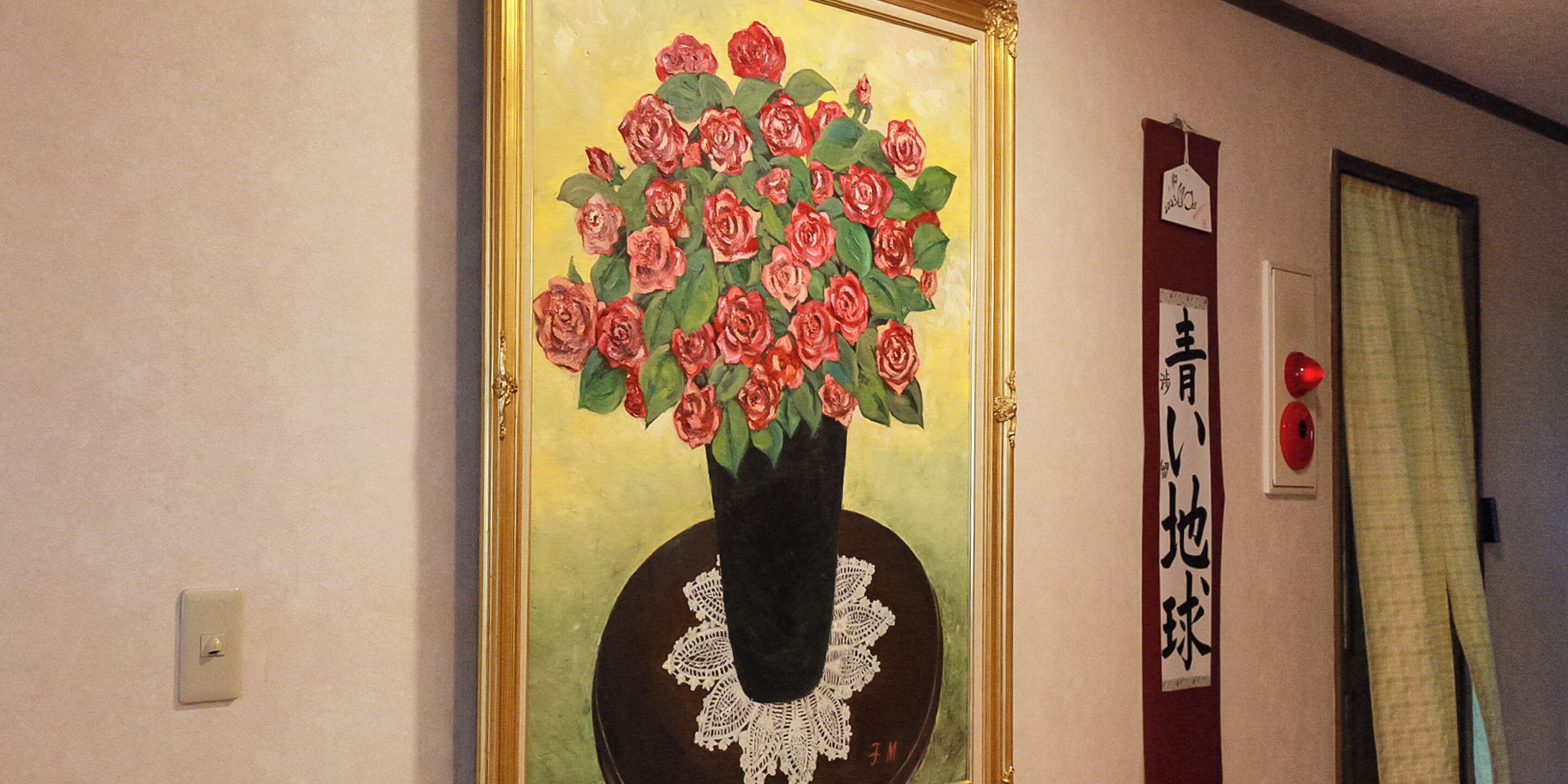 Un cuadro enmarco con un jarrón de rosas rojas sobre una pared.