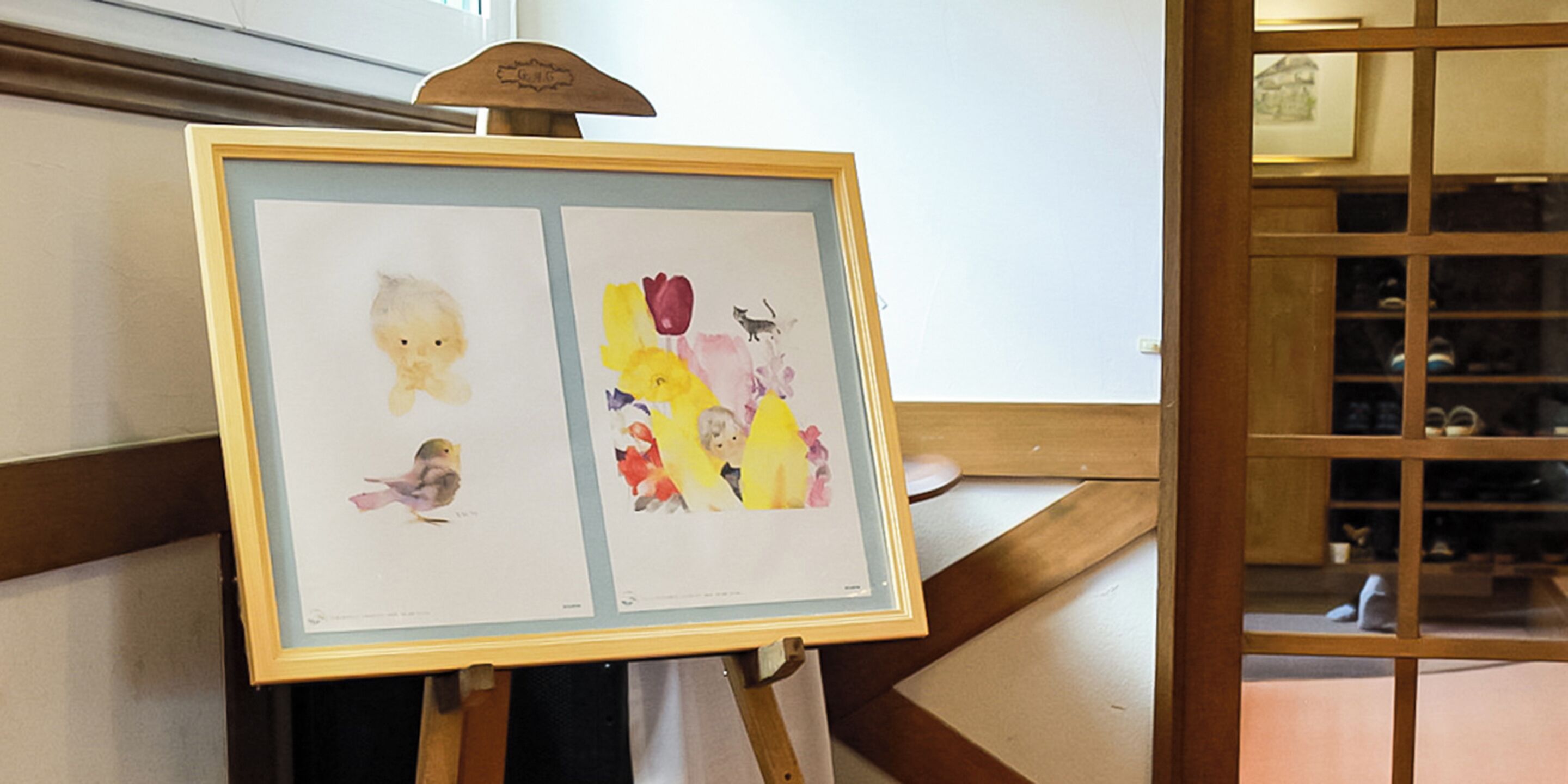 A framed artwork on an easel in a room with wooden paneling and a window.