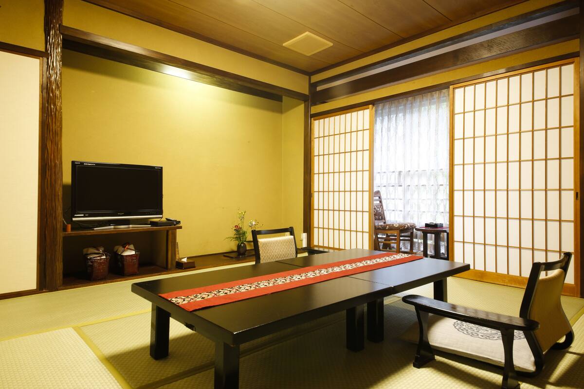 Een traditionele Japanse kamer met tatami vloerbedekking, een lage tafel, een televisie en schuifdeuren.