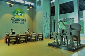 Zona de recepción con el logotipo de 'The Mountain Courtyard', un mostrador de recepción, dos sillas y una escultura de elefantes.