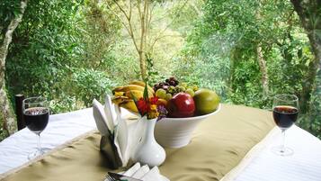 A table set with a fruit bowl, two wine glasses, and a vase with flowers.