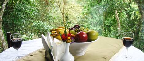 A table set with a fruit bowl, two wine glasses, and a vase with flowers.