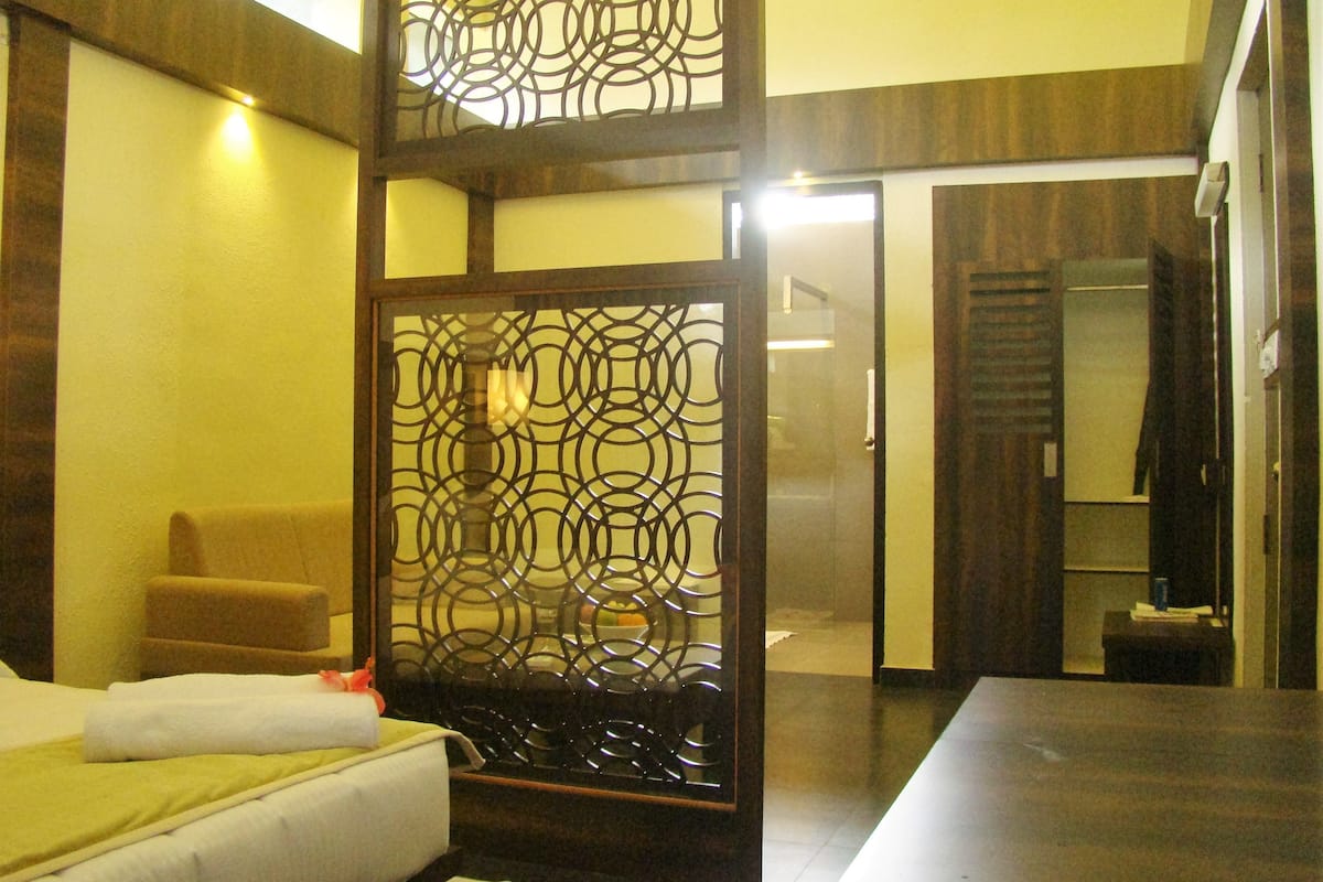 A hotel room with a bed, a chair, a decorative screen, and a bathroom visible through an open door.