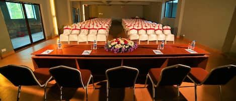 A conference room with a long table, white chairs with red sashes, and a floral centerpiece.