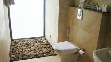 Un baño con inodoro, lavamanos, ducha y ventana con vista a rocas.