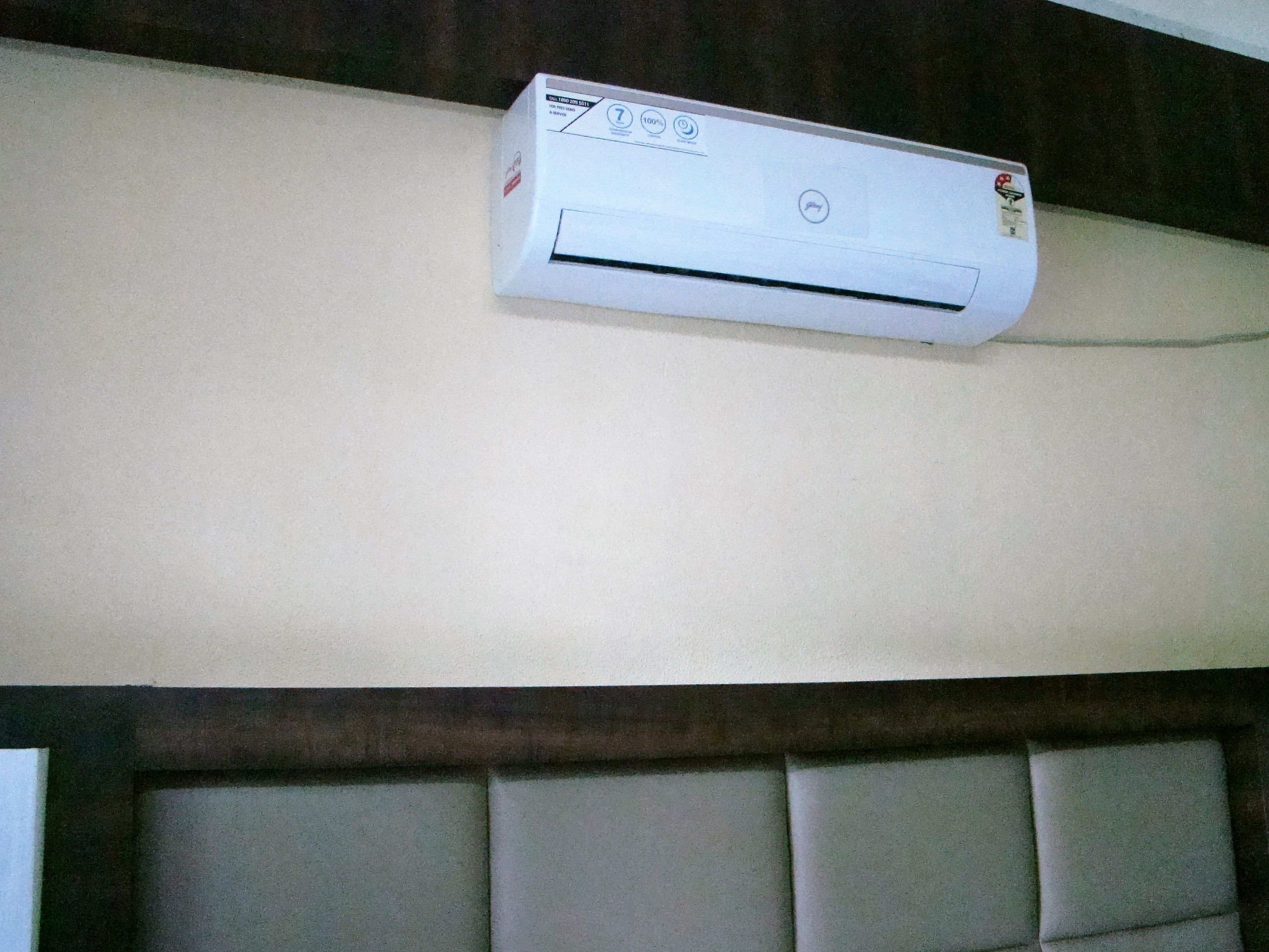 A white air conditioning unit mounted on a wall above a padded headboard.
