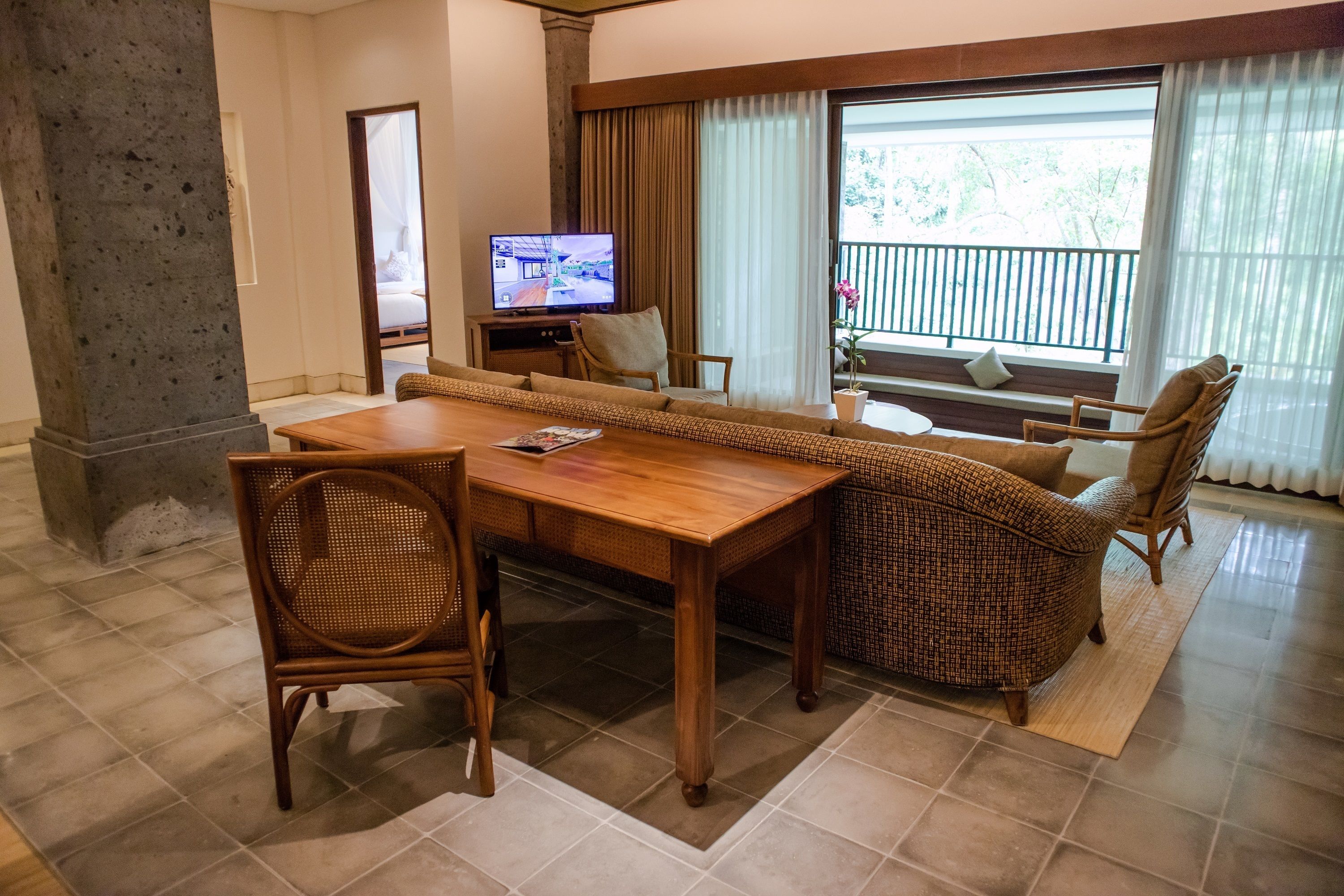 A spacious living area with a wooden dining table, wicker sofa, and a television.