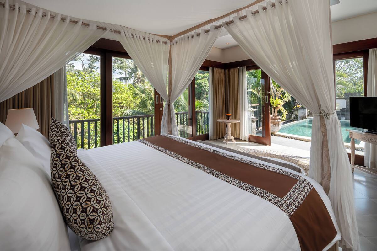 A spacious bedroom with a large bed, a TV, and a balcony with a pool view.
