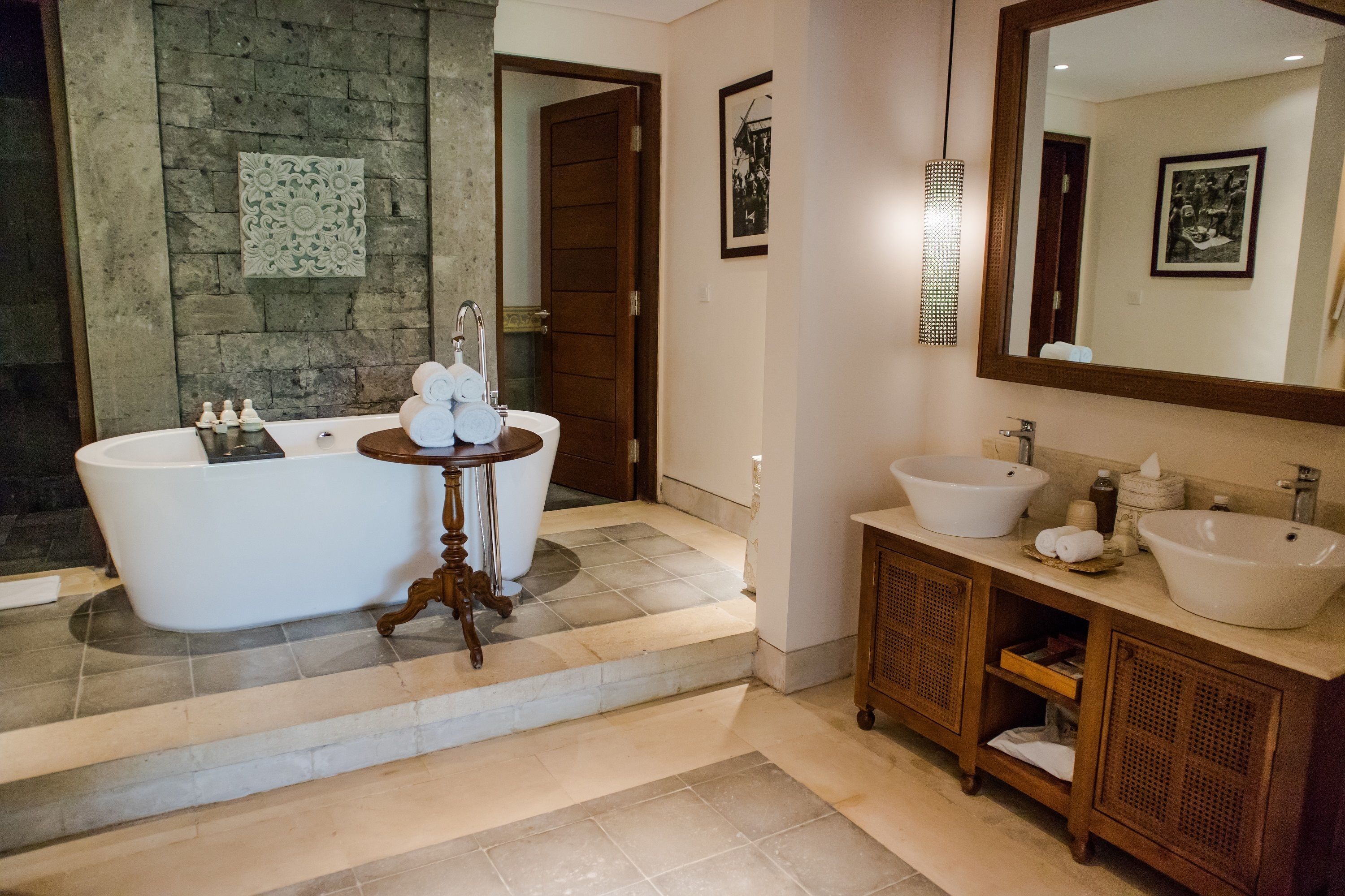 A bathroom with a freestanding bathtub, a vanity with a large mirror, and a stone wall.