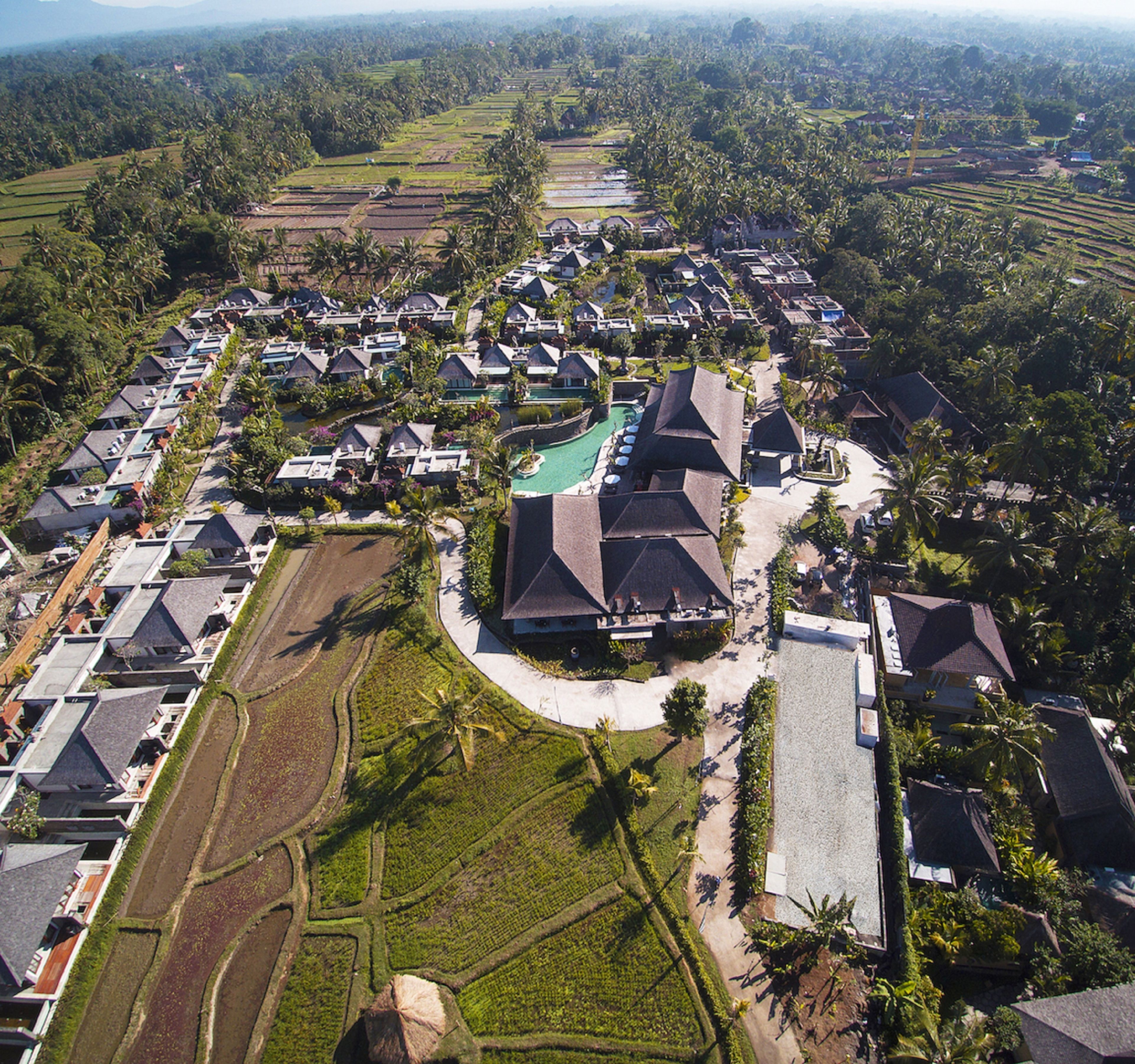An aerial view of a resort with multiple bungalow-style buildings, a central pool area, and surrounding agricultural fields.