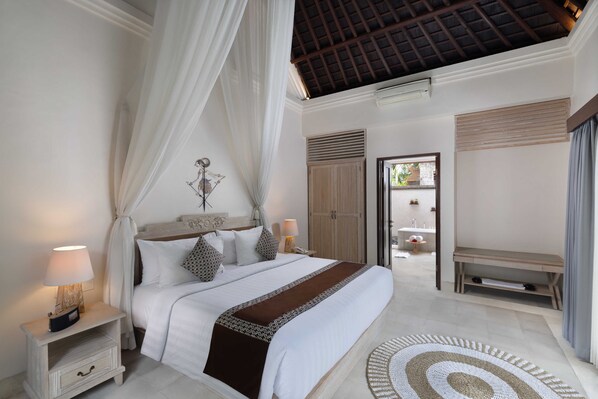 A bedroom with a bed, bedside tables, a bench, and a view of the bathroom. - Visesa Ubud Resort (Ubud)