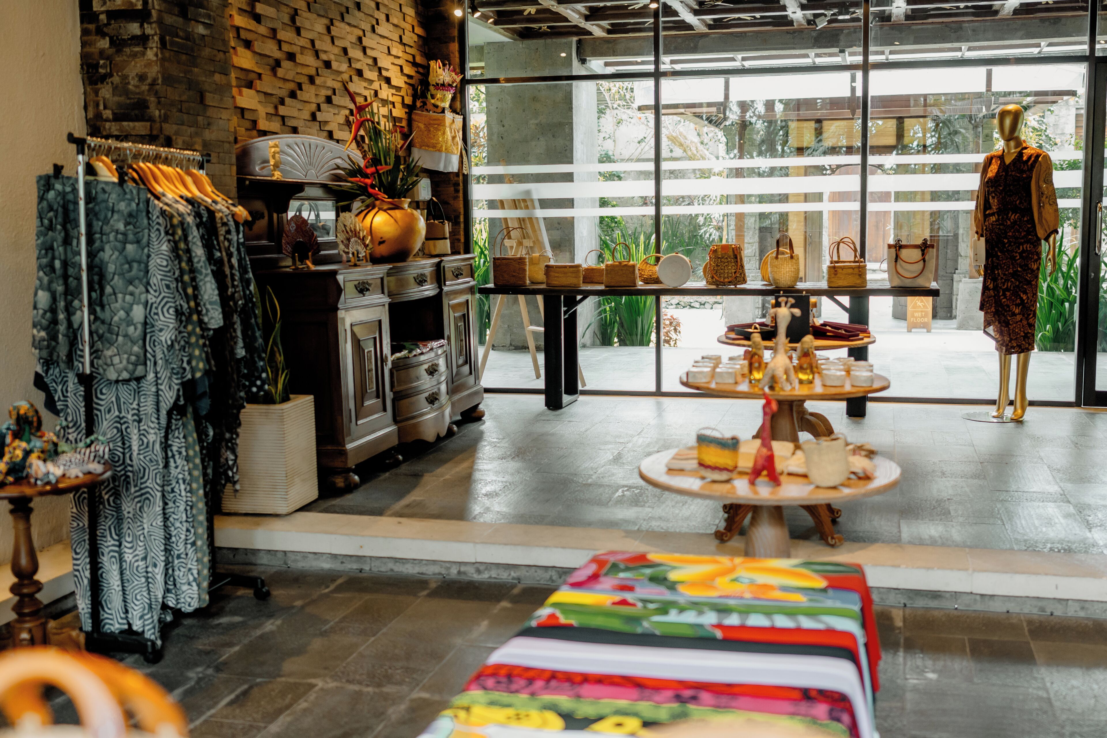 Interieur van een boetiekhotel met een bakstenen muur, een etalagepop, een presentatie van handtassen en een tafel met etenswaren.