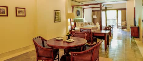 Un comedor con una mesa redonda y sillas de mimbre, una cama con dosel al fondo y vistas del salón.