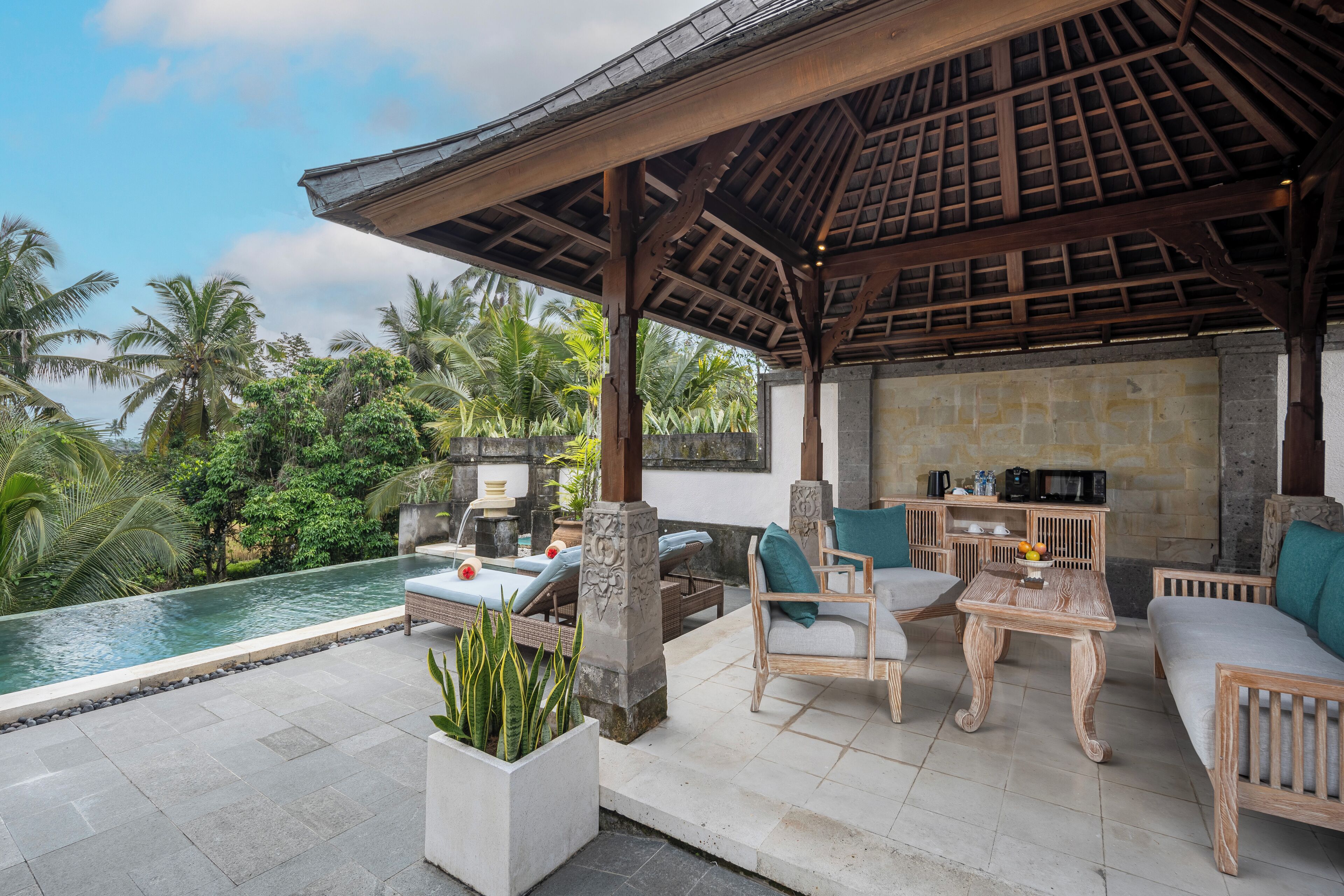 A covered outdoor area with a pool, seating, and a stone wall.