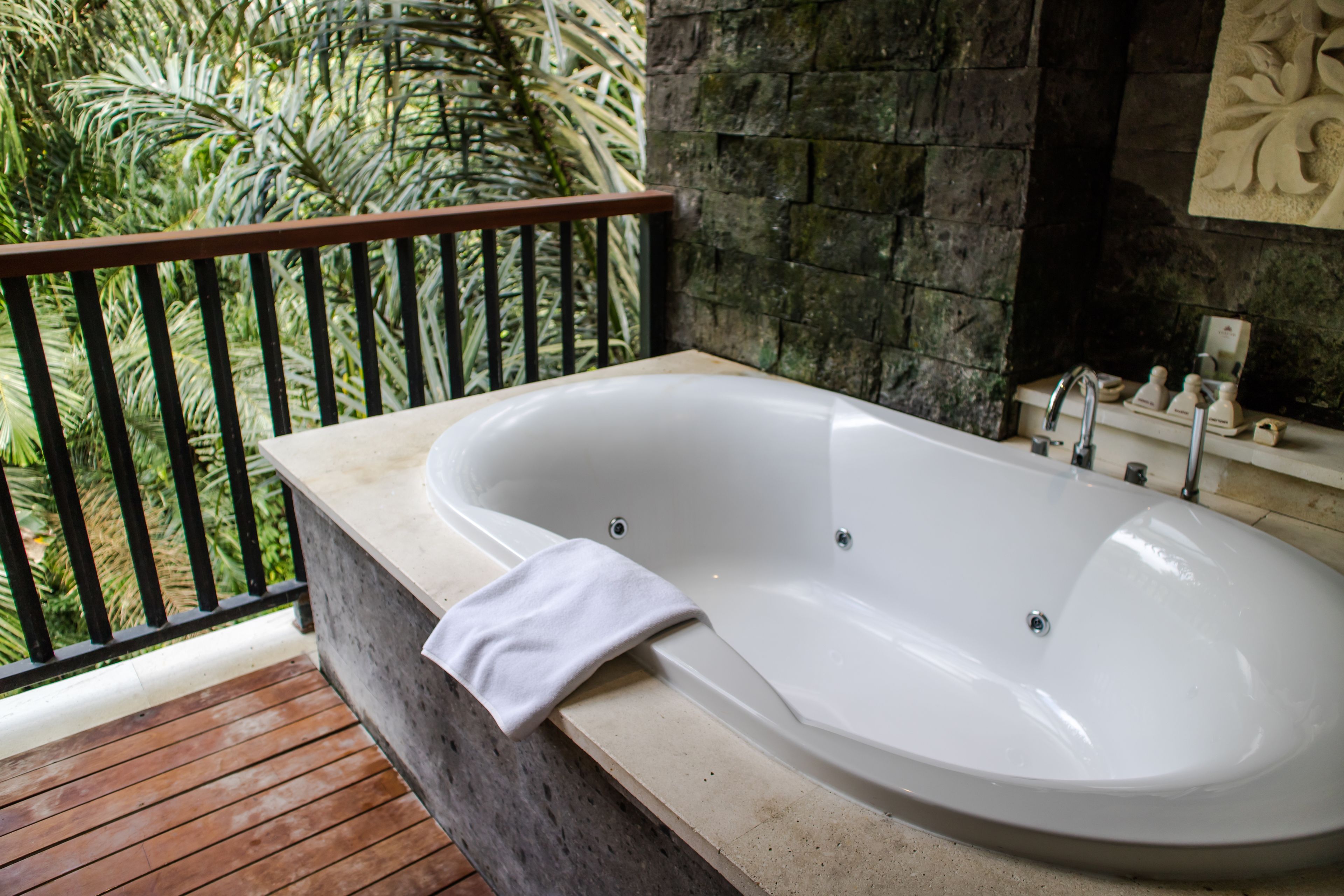 A spa bathroom with a freestanding bathtub, a stone wall, and a wooden deck with a railing.
