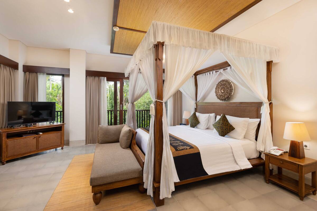 A spacious bedroom with a four-poster bed, a television, and a bedside table with a lamp.