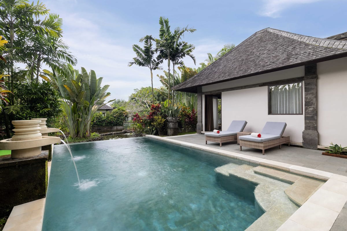 A swimming pool with two lounge chairs, surrounded by tropical plants and a small waterfall feature.