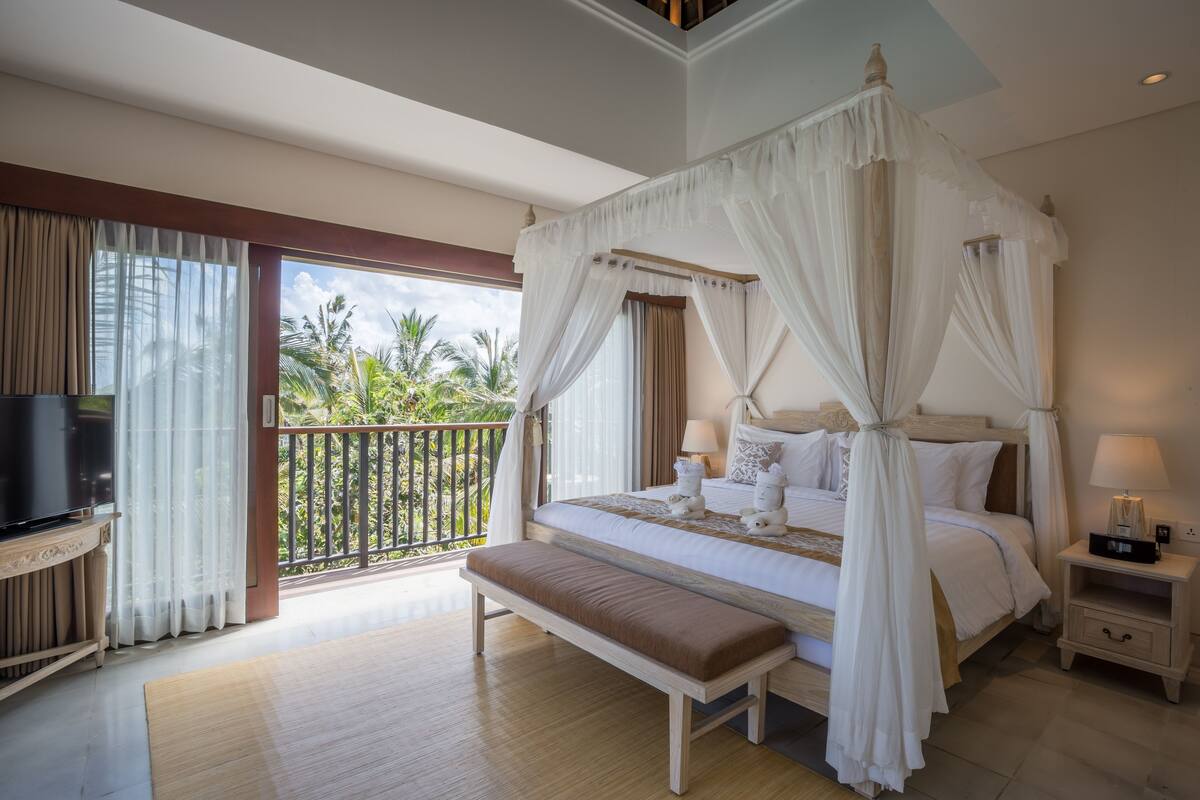 A spacious bedroom with a large bed, a bench, a bedside table, and a TV.