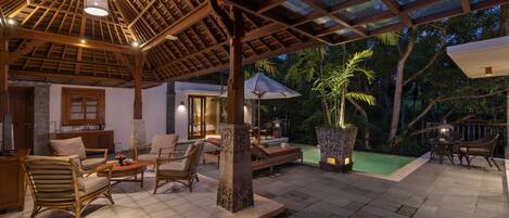 An outdoor patio area with wooden furniture, a pool, and a covered seating area.
