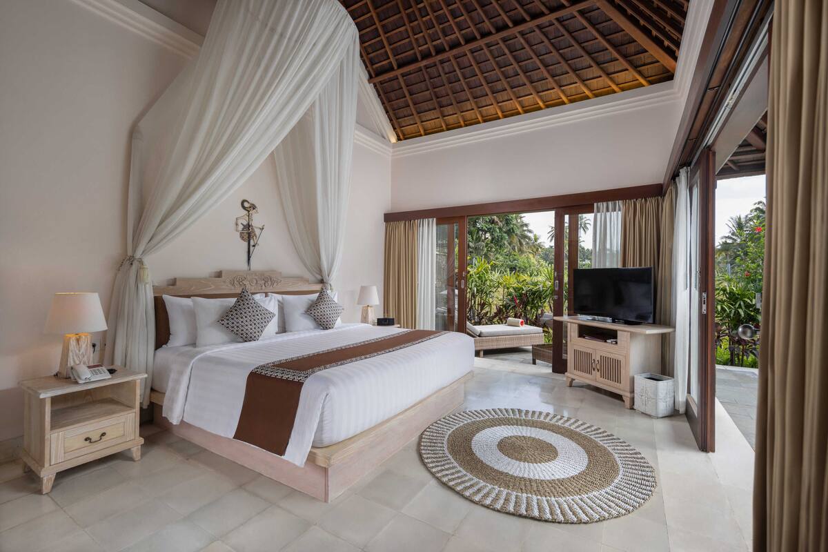 A bedroom with a large bed, a TV, and a view of greenery outside.