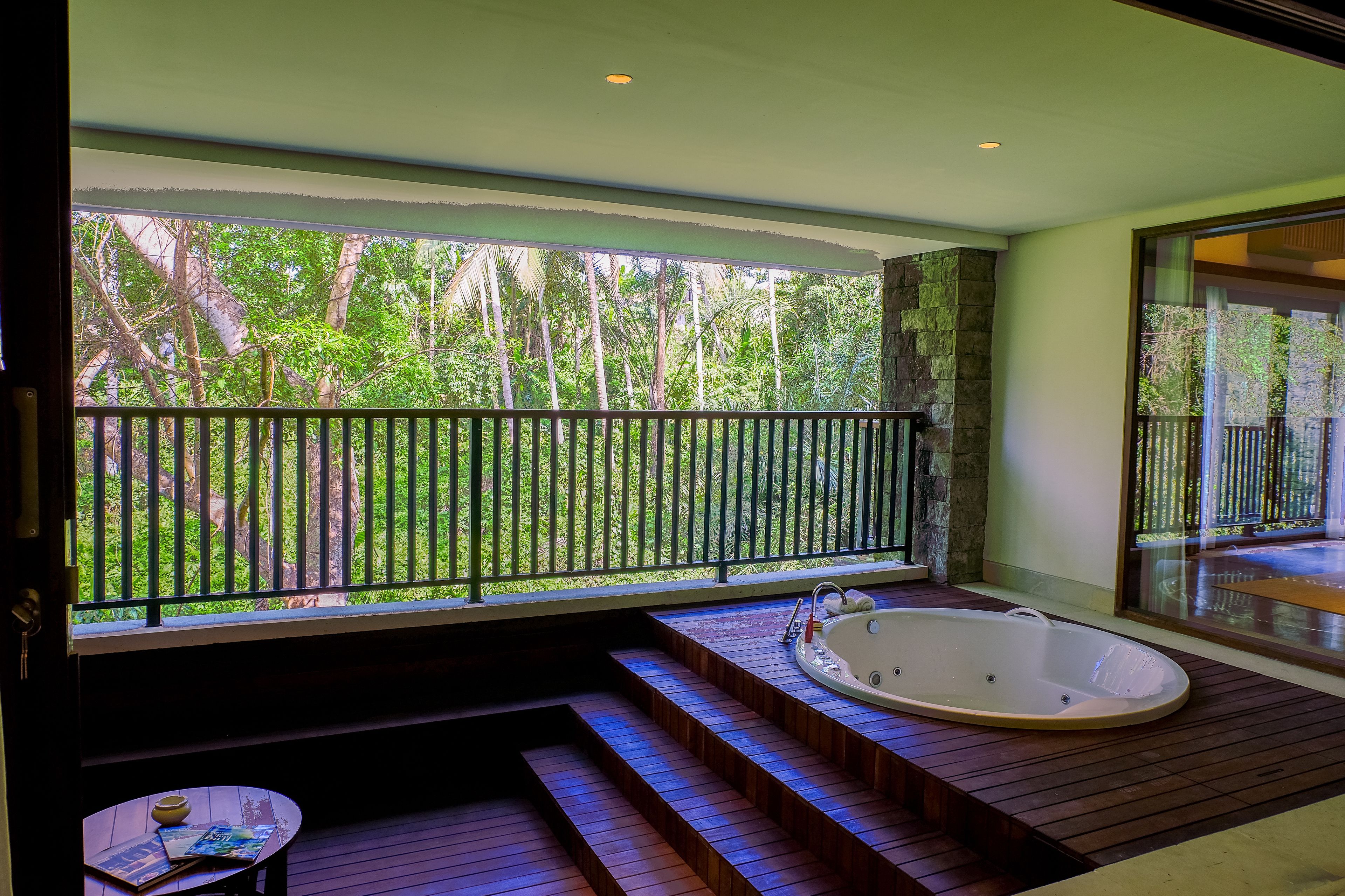 Ein Wellnessbereich mit Whirlpool, Holzstufen und Blick auf einen üppigen Garten durch einen Balkon.
