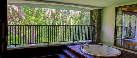 Ein Wellnessbereich mit Whirlpool, Holzstufen und Blick auf einen üppigen Garten durch einen Balkon.