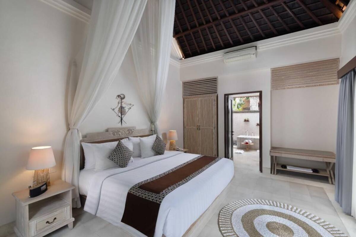 A bedroom with a canopy bed, bedside tables, a bench, and a view of the outside.
