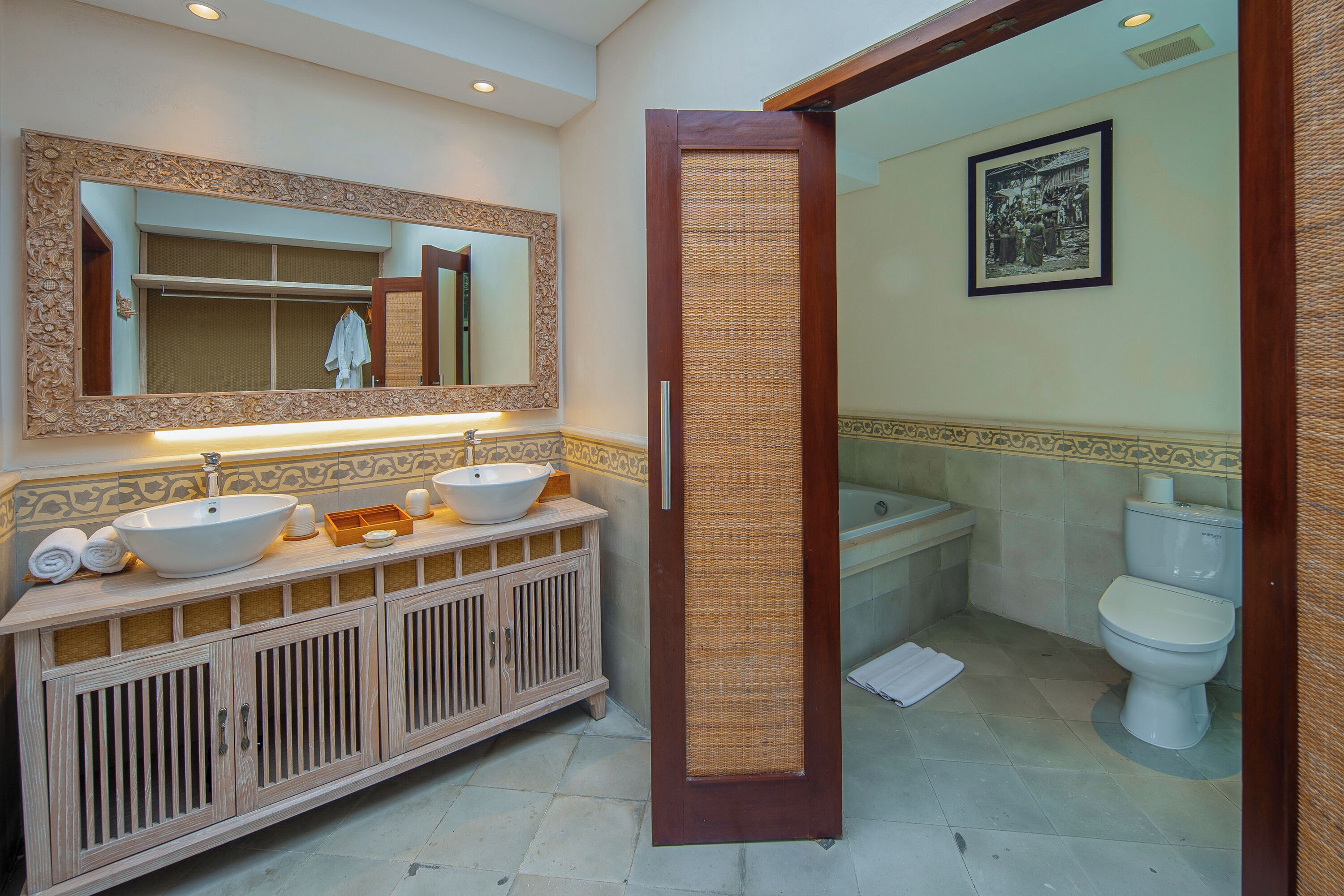 A bathroom with a wooden vanity, two sinks, a mirror, a toilet, and a shower area.