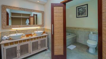 A bathroom with a wooden vanity, two sinks, a mirror, a toilet, and a shower area.