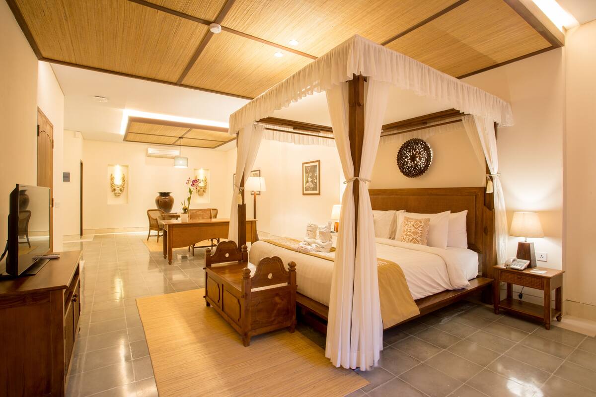 A spacious bedroom with a four-poster bed, a wooden desk, and a dining area.