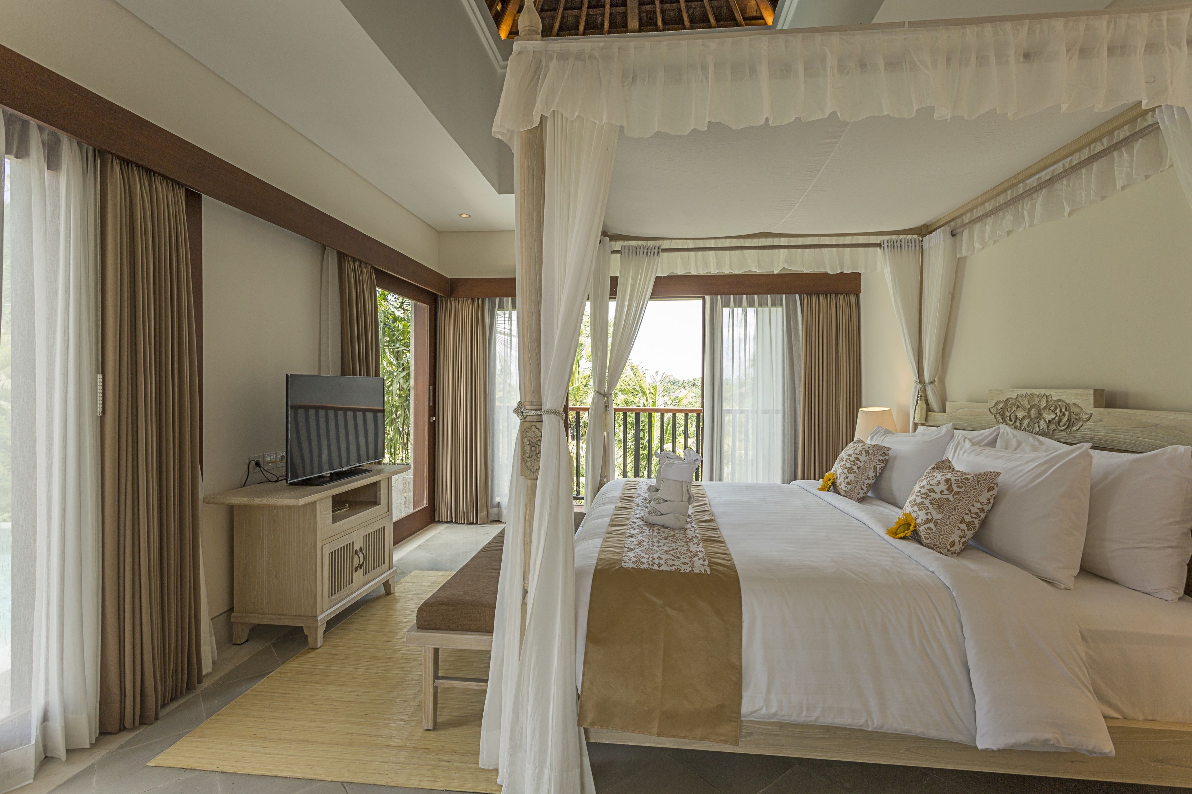 Una camera da letto con un letto a baldacchino, una televisione su un supporto in legno e un balcone con tende.