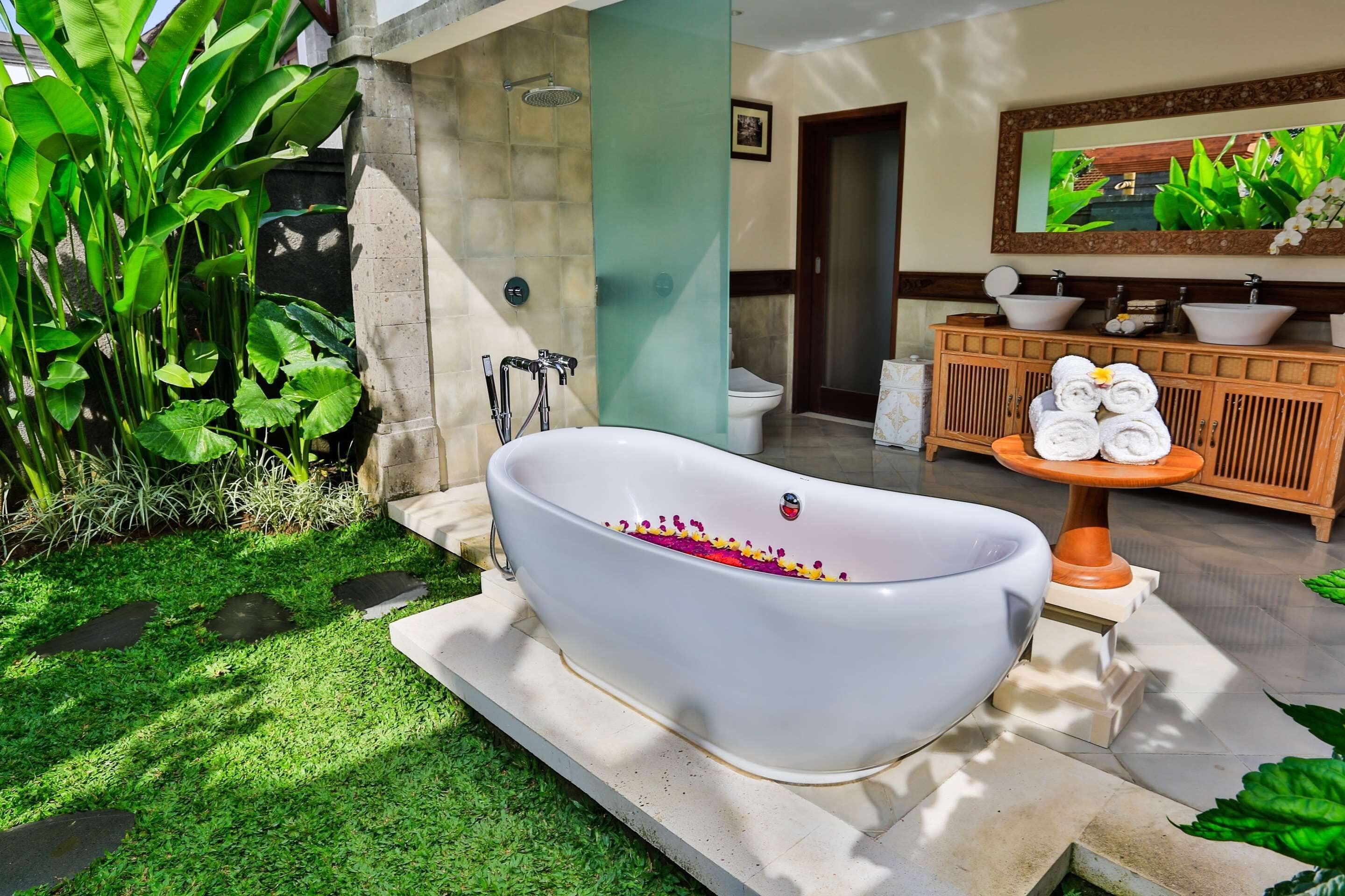 Eine freistehende Badewanne mit Duschbrause, ein Holzkosmetikschrank mit zwei Waschbecken und ein Spiegel darüber.