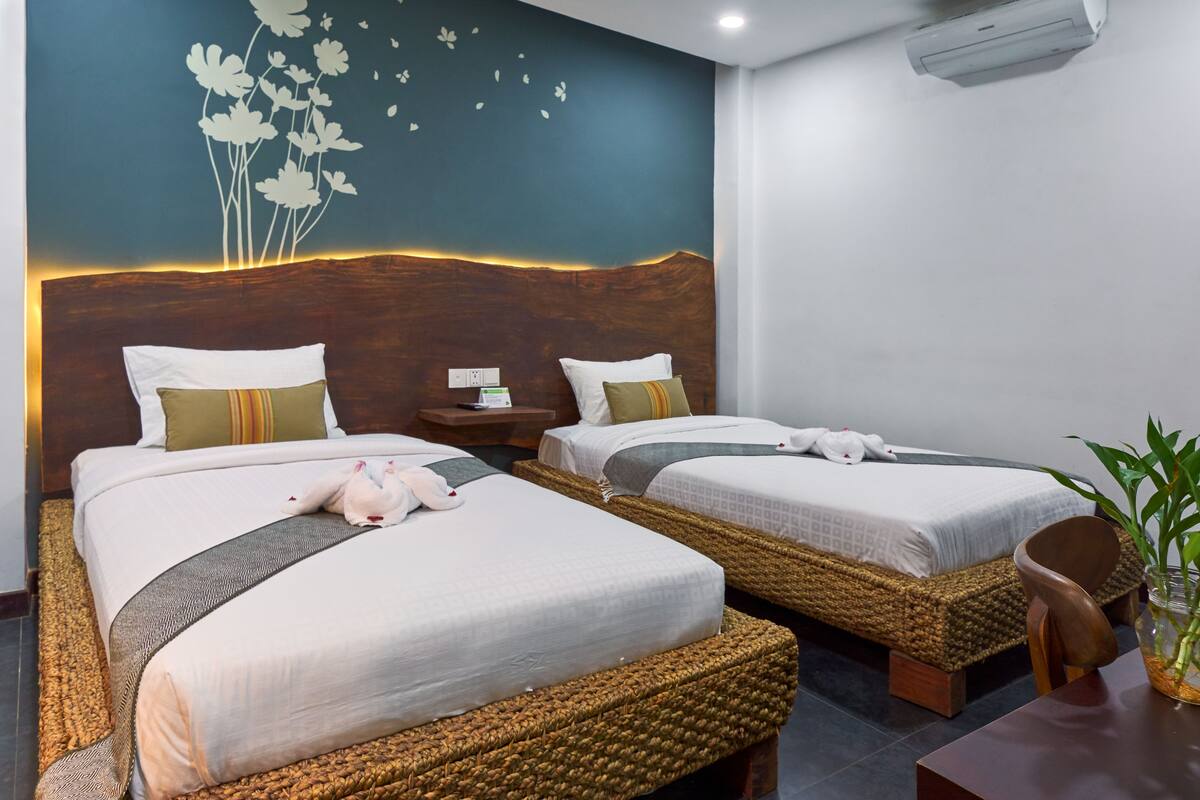 Habitación de hotel con dos camas, una mesita de noche, aire acondicionado montado en la pared y una planta en maceta.
