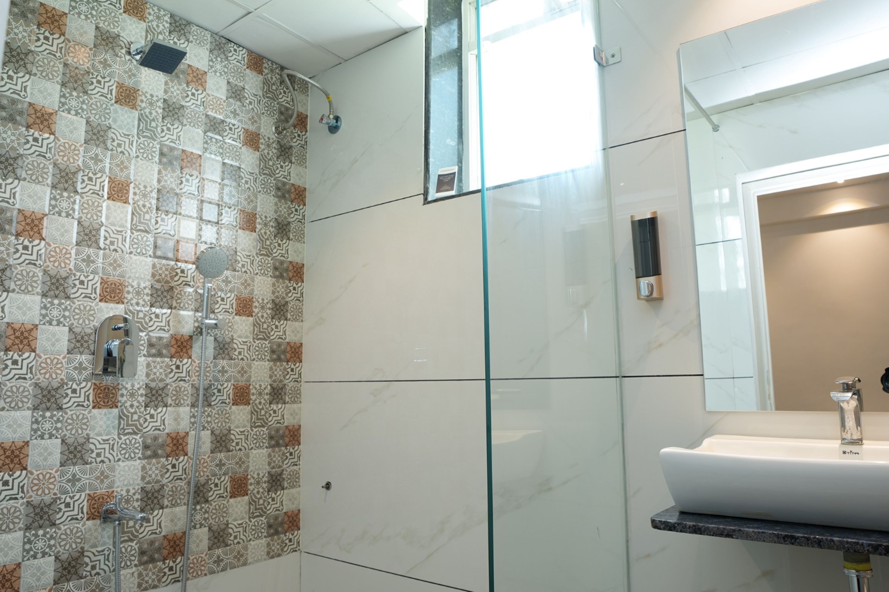 A modern bathroom with patterned tiles, a glass shower enclosure, a marble countertop, and a large mirror.