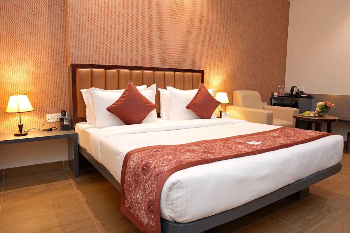 Ein Hotelzimmer mit einem großen Bett, zwei Nachttischen, einem Sessel, einem kleinen Tisch mit Blumen und einer Wand mit strukturierter Oberfläche.