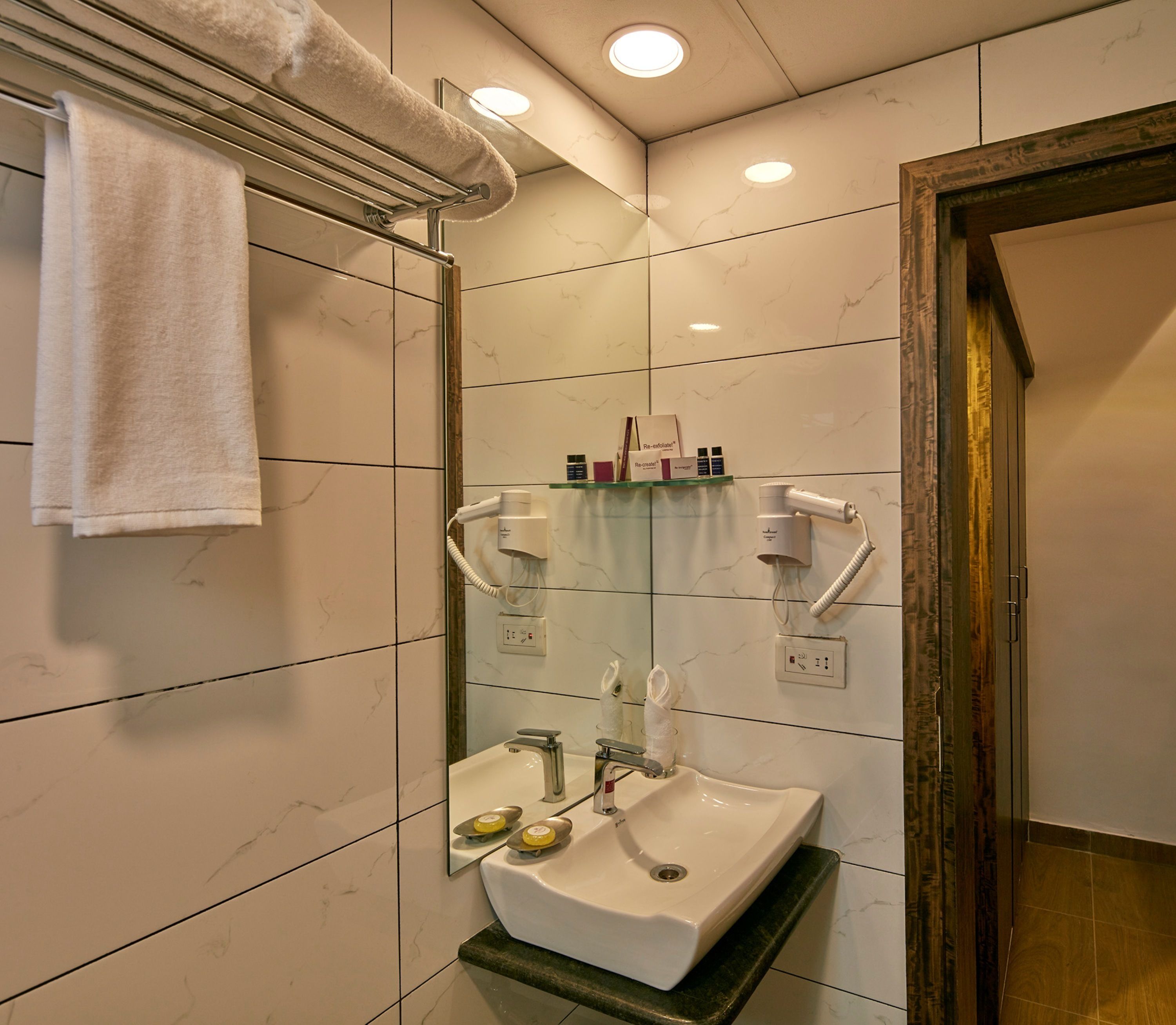 A bathroom with a sink, mirror, towel rack, and a shower area.