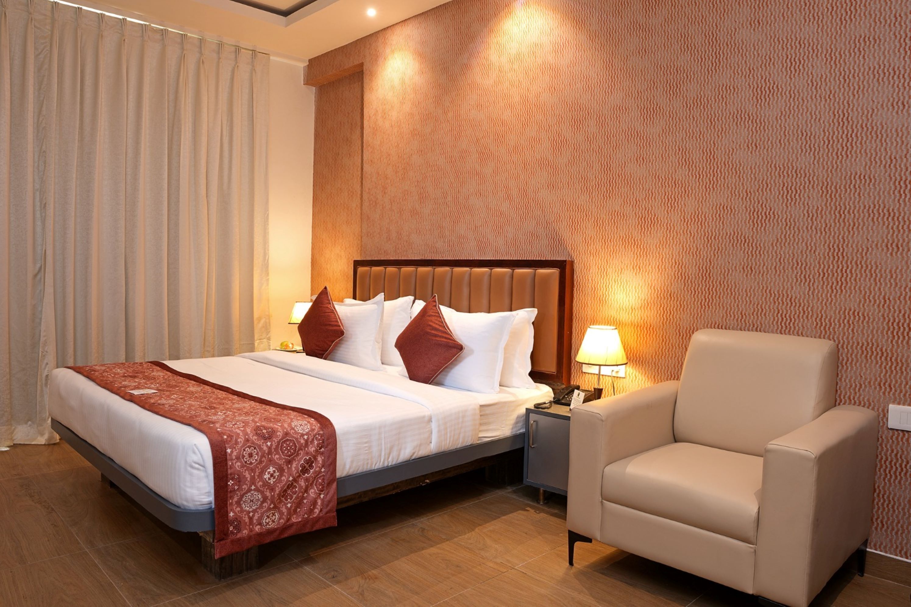 A hotel room with a bed, a nightstand, a chair, and a patterned wall.