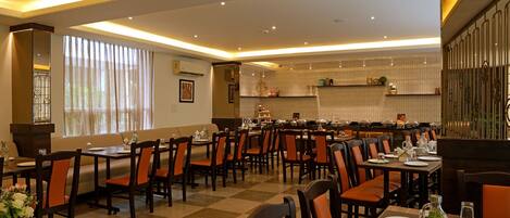 A restaurant with multiple dining tables and chairs, a checkered floor, and a warm, well-lit interior.