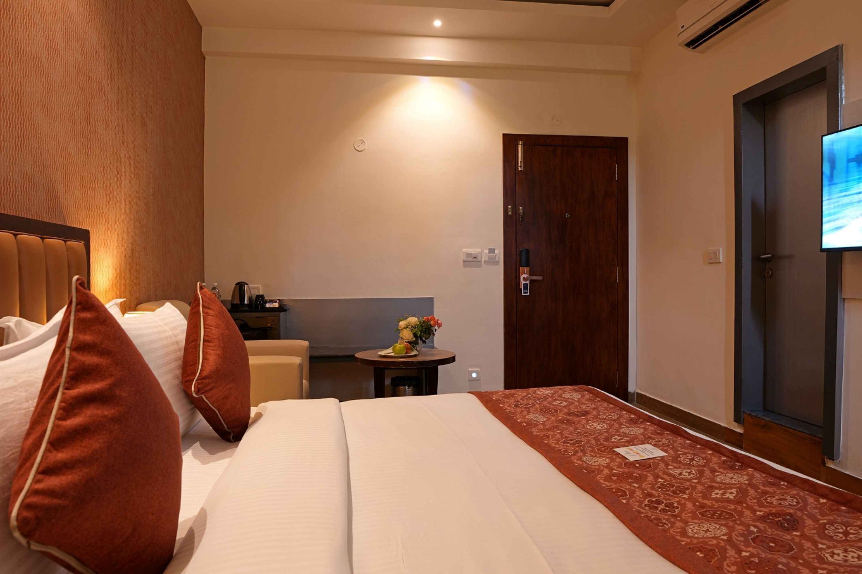 Habitación de hotel con una cama, una mesita con un florero, un escritorio y un televisor montado en la pared.