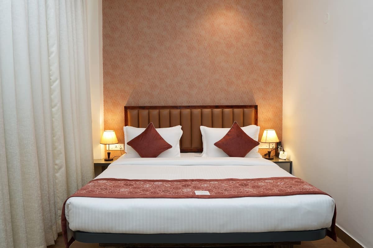 Ein ordentlich bezogenes Bett mit weißen Laken und zwei braunen Kissen, beides flankiert von jeweils einer Nachttischlampe auf passenden Nachttischen.