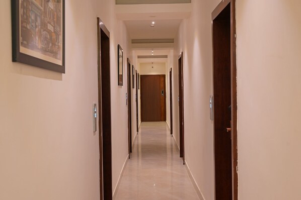 Un pasillo de hotel con varias puertas, cuadros en las paredes y un suelo de color claro.