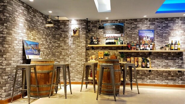 Een bar met bakstenen muren, houten krukken en diverse flessen op planken.