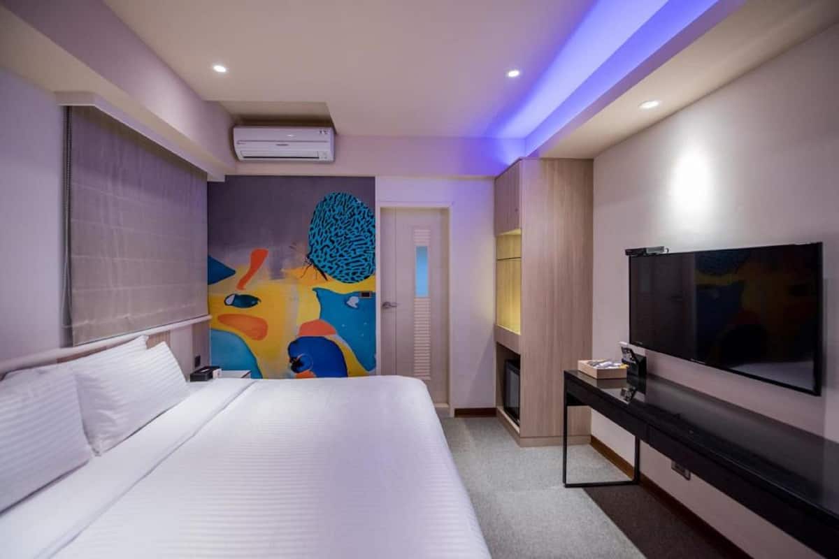 A modern hotel room with a large bed, a flat-screen TV mounted on the wall, and a colorful abstract mural on the wall.