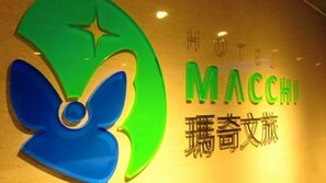 Un letrero de hotel con un gran logotipo verde y azul, y el nombre 'HOTEL MACCHI' en letras verdes.