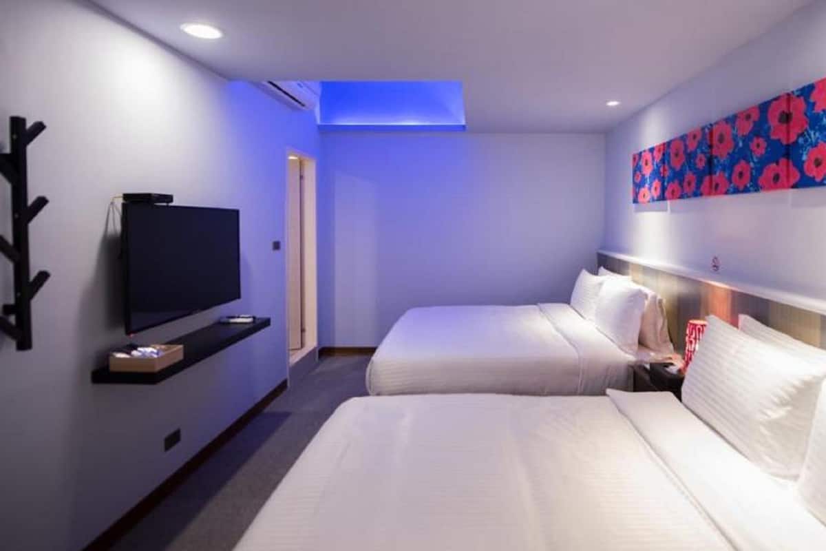 A hotel room with two beds, a flat-screen TV, a painting on the wall, and a ceiling light.
