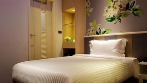 Een opgemaakt bed met een witte dekbedovertrek en kussens, een houten garderobe en een wand met een bloemmotief.